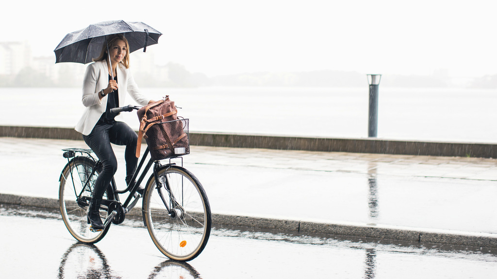 Kvinna håller i ett paraply samtidigt som hon cyklar i regnet.