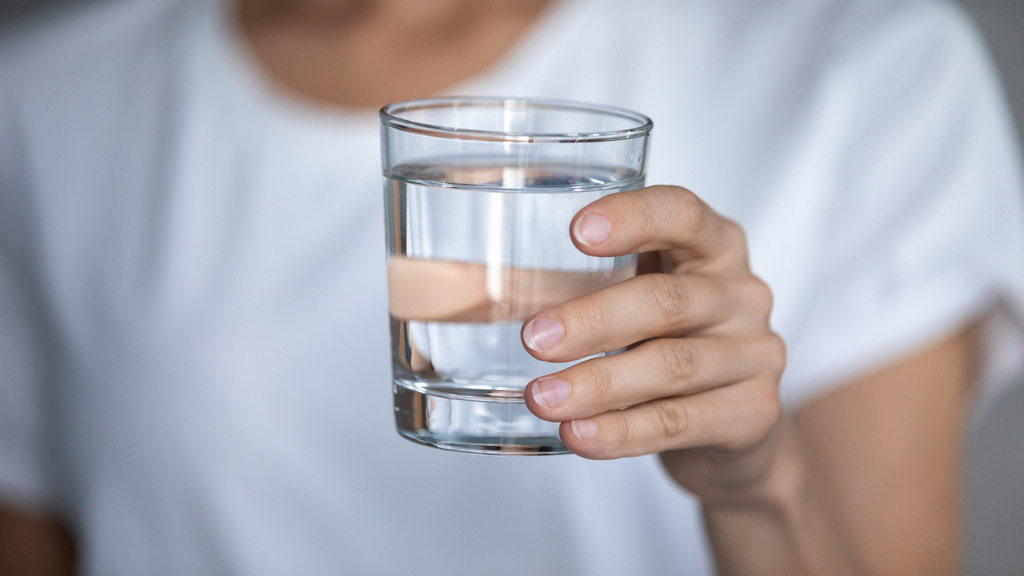 En person som inte visar sitt ansikte håller upp ett glas med rent vatten.