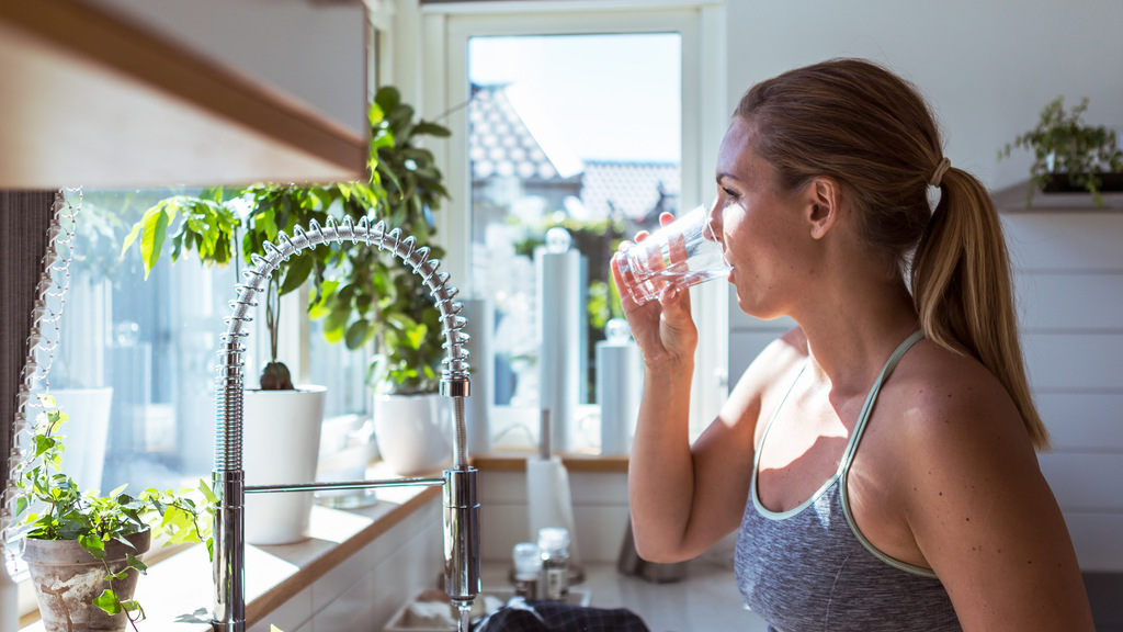 Kvinna står vid diskbänk och dricker ett glas vatten.