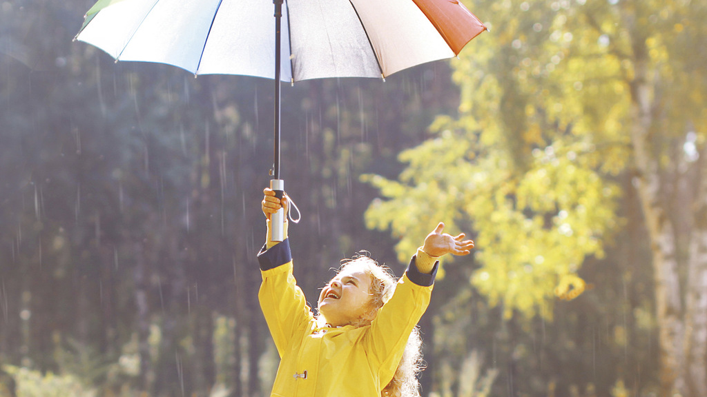 Positive child with colorful umbrella having fun in autumn day