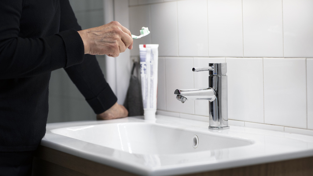 En hand håller i en tandborste, bakom en avstängd vattenkran.